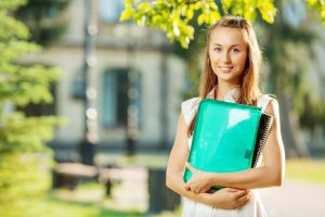 Student woman is standing with the folder and copy-book on the u